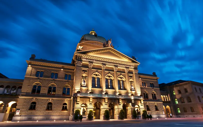 Beleuchtete Fassade des Bundeshauses in Bern vor dunkelblauem Abendhimmel