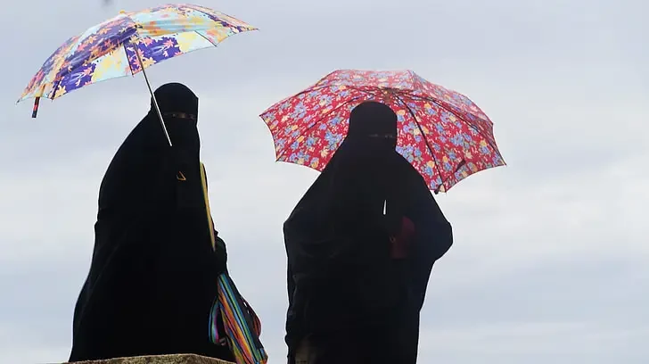 Zwei Personen in schwarzen Gewändern und Gesichtsschleiern halten bunte Regenschirme
